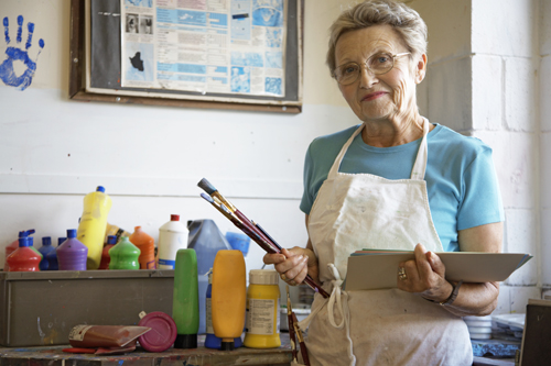 Mature woman in art classroom, holding brushes and paper, portrait