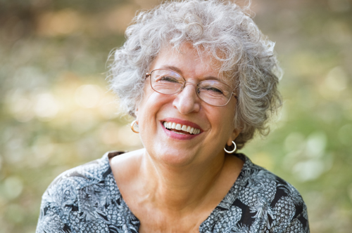 Portrait of senior woman smiling and looking at camera. Cheerful mature woman wearing eyeglasses in the park. Happy old woman with grey hair smiling. Carefree and positive retired woman.