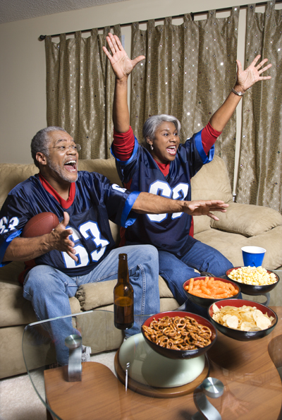 Mature African-American couple cheering and watching football game at their home on television.