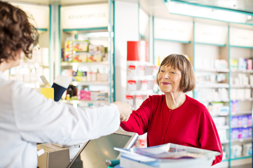 Senior female customer standing at chemist counter as pharmacist hands her medication order