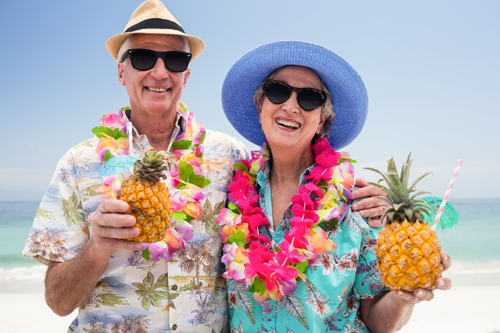 Happy senior couple wearing a garland and holding pineapple cocktail at the beach