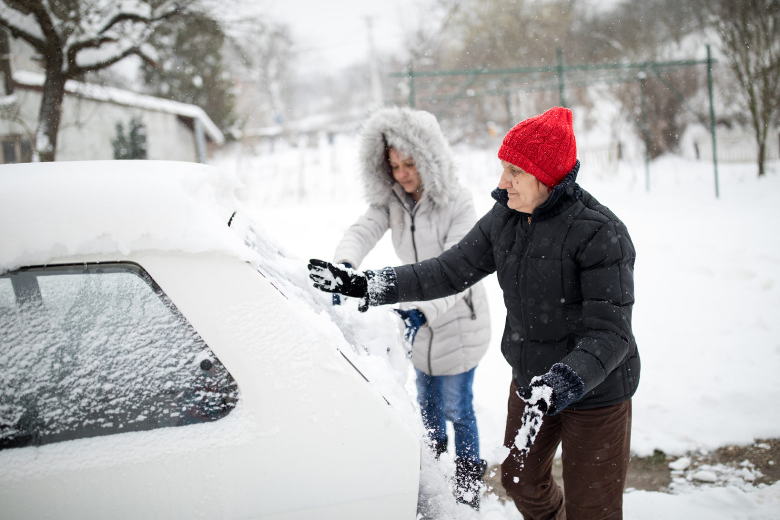A women cleans a snow-covered car. Around the big snowdrifts.Stuck in snow.