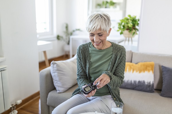 Happy mature woman with glucometer checking blood sugar level at home. Woman testing for high blood sugar. Woman holding device for measuring blood sugar