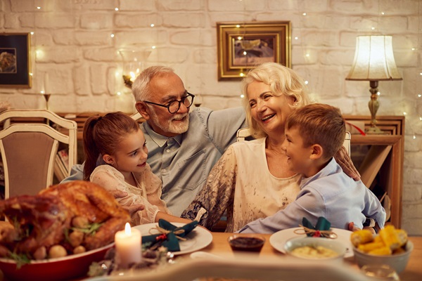 Happy grandparents talking to their grandchildren during Thanksgiving meal at dining table at home.