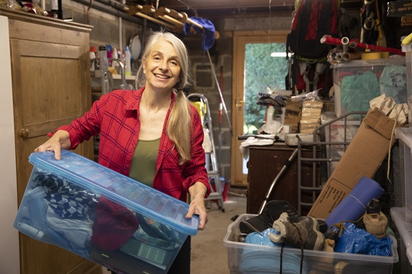 A mature woman smiles as she carries boxes of belongings to sort through whilst in lockdown at home.