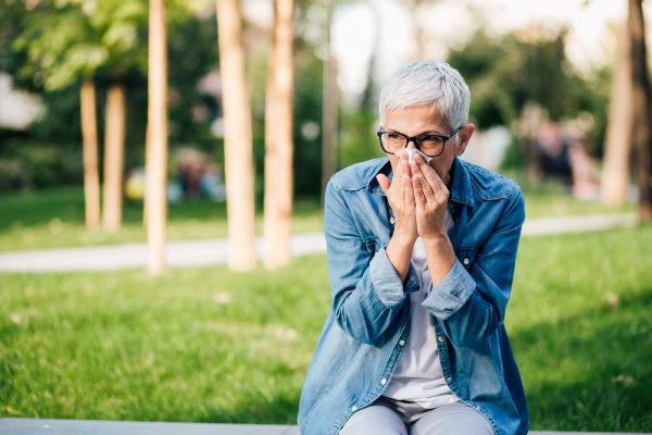Older woman blows nose outside
