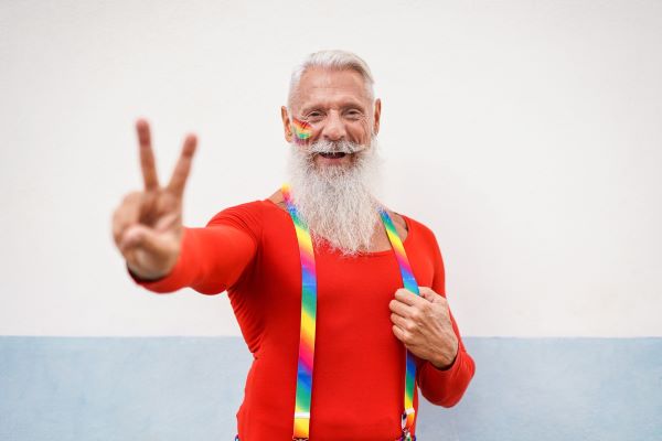 Adult senior dressed in rainbow suspenders gives peace sign with fingers