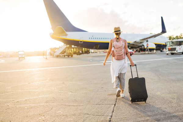 Woman in resortwear walks toward plan with suitcase