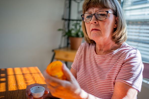 Older adult woman reads the back of a pill bottle