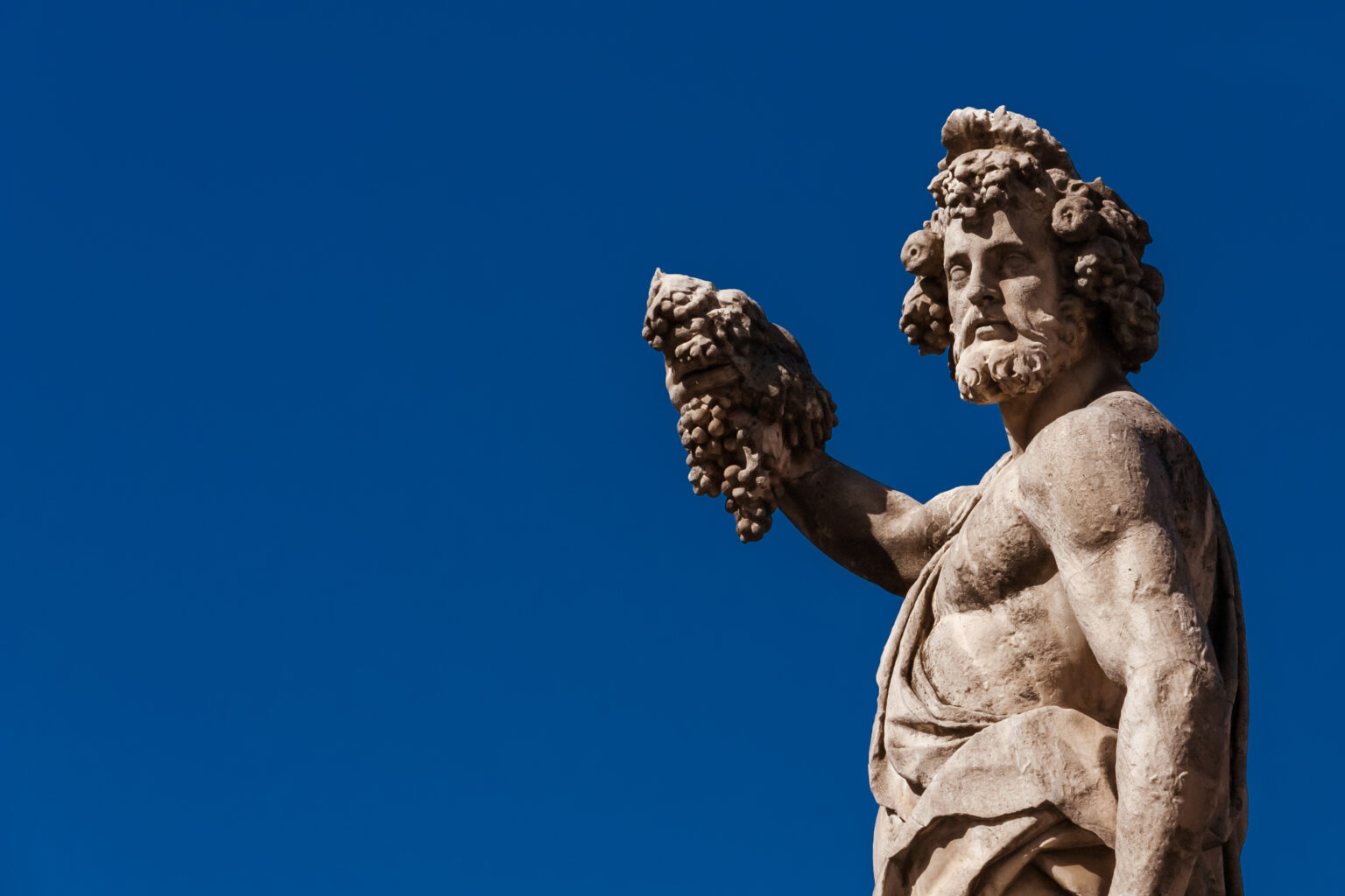 Paganism in Ancient Times. Roman or Greek god Bacchus holding grapes, a baroque statue, erected in the 17th century on Holy Trinity Bridge in Florence historic center