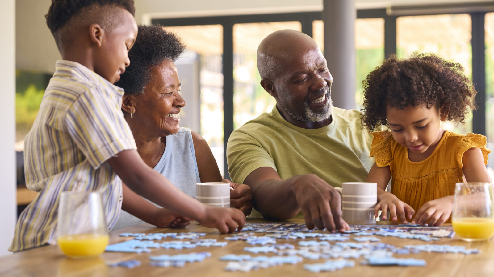 Family Shot With Grandparents And Grandchildren Doing Jigsaw Puzzle On Table At Home