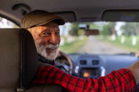 Portrait of senior man driving car in reverse and looking over shoulder